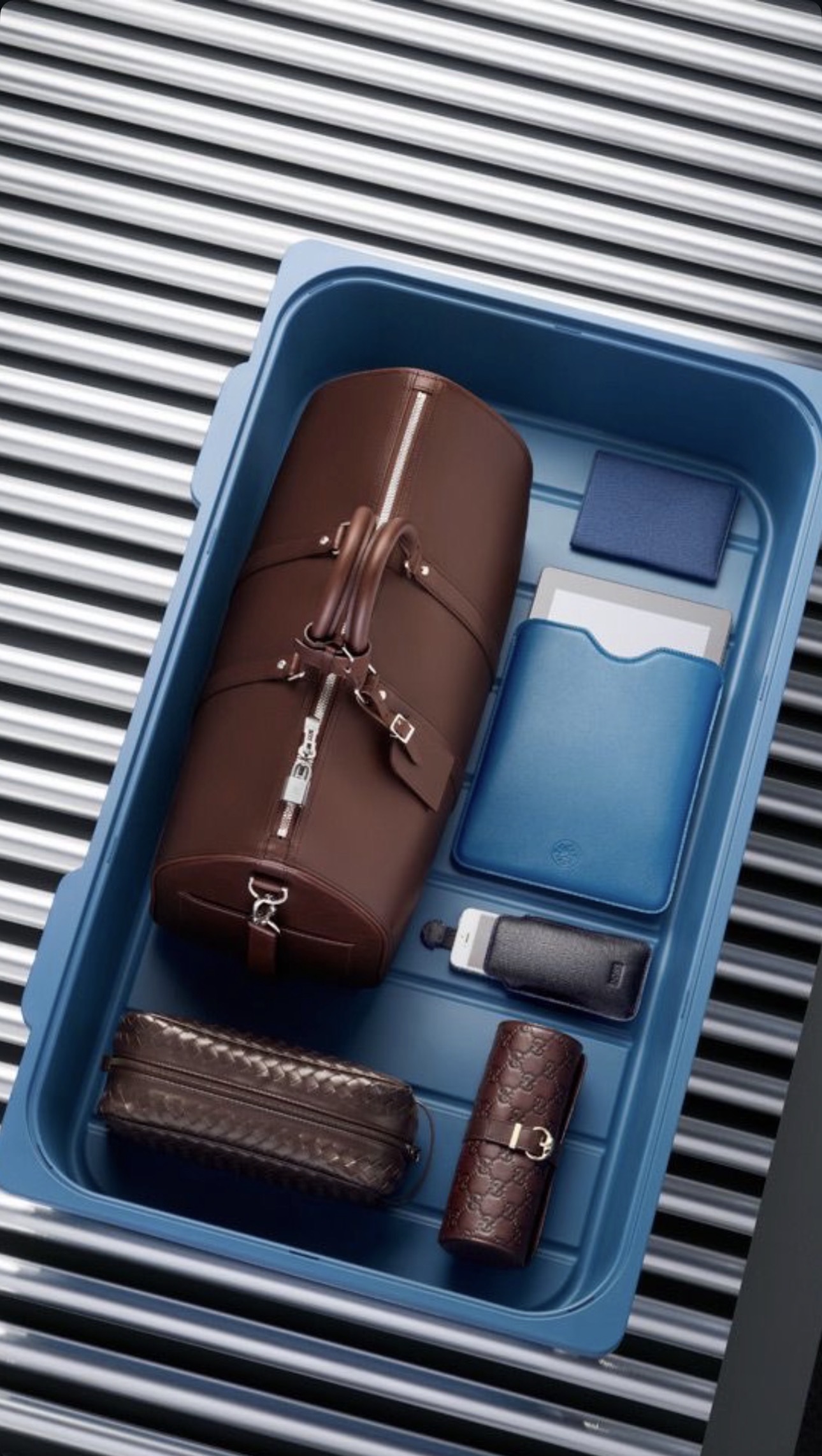 Travel duffel and leather accessories in a blue airport security bin